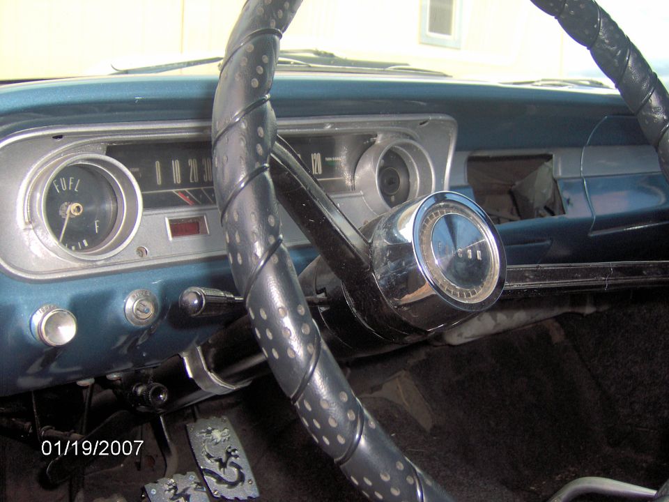 Dashboard view of a car with a fuel gauge and speedometer. Steering wheel is black with a chrome horn button