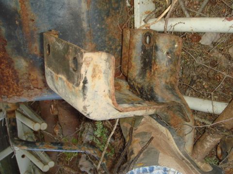 1996 Ford Bronco - Close-up view of heavily rusted metal brackets, likely from a vehicle's undercarriage, amidst outdoor debris.