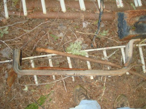 1996 Ford Bronco - A close-up view of a rusted metal part lying on the ground amidst forest debris.