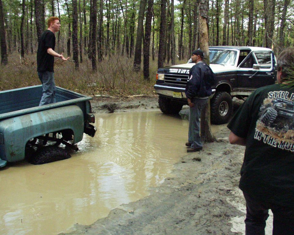 Ford Bronco and a pickup truck stuck in a muddy forest clearing