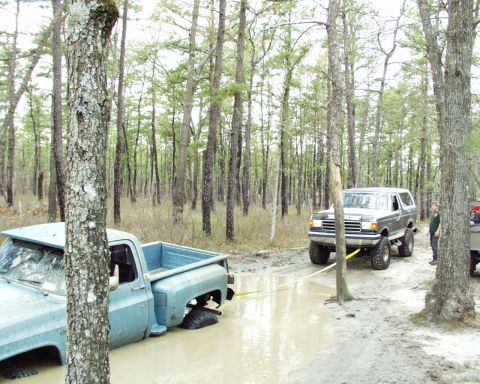 1989 Ford Bronco - A Ford Bronco tows a stuck pickup truck from a muddy clearing surrounded by trees.