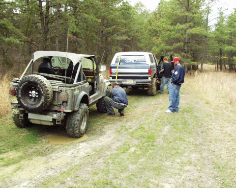 1989 Ford Bronco - A blue Ford Bronco is parked on a dirt road while people work on a nearby Jeep.