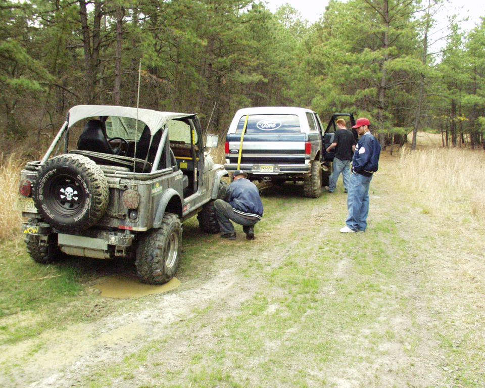 Blue Ford Bronco with a yellow pole attached to the rear, parked on a dirt road
