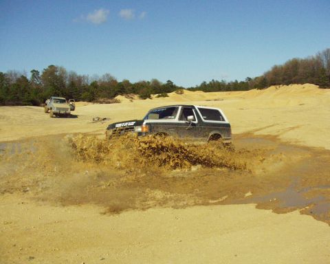 1989 Ford Bronco - A 1989 Ford Bronco splashes through a muddy area with another vehicle visible in the distance.