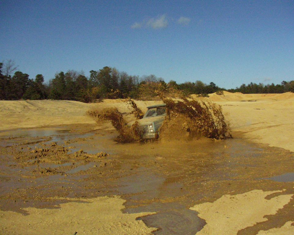 Light-colored SUV splashing mud while driving through a muddy area