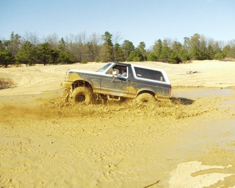 1989 Ford Bronco - A 1989 Ford Bronco navigates a muddy off-road course, kicking up a spray of dirt.