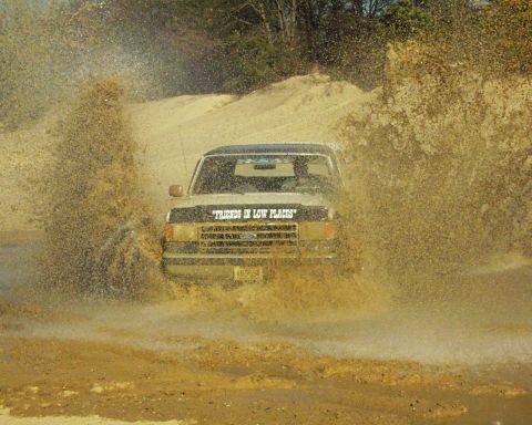 1989 Ford Bronco - A Ford truck navigates a muddy obstacle, sending water flying.
