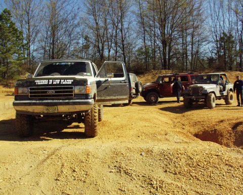1989 Ford Bronco - Several off-road vehicles, including a Ford pickup, Hummer, and Jeep, are gathered on a dirt track.