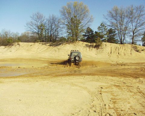 1989 Ford Bronco - A 1989 Ford Bronco navigates a muddy off-road course under a clear blue sky.