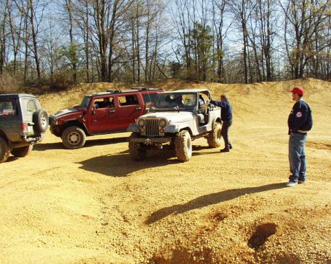 1989 Ford Bronco - Several off-road vehicles are gathered on a dirt terrain, with people interacting near one of the Jeeps.