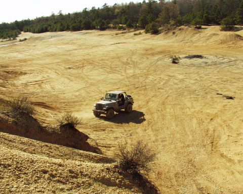 1989 Ford Bronco - A gray Jeep CJ-7 navigates a sandy, off-road landscape with trees in the background.