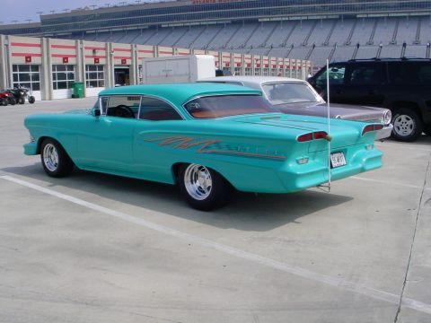 1972 Ford Ranchero - A turquoise 1958 Plymouth Fury with custom flame decals is parked in front of a racetrack grandstand.
