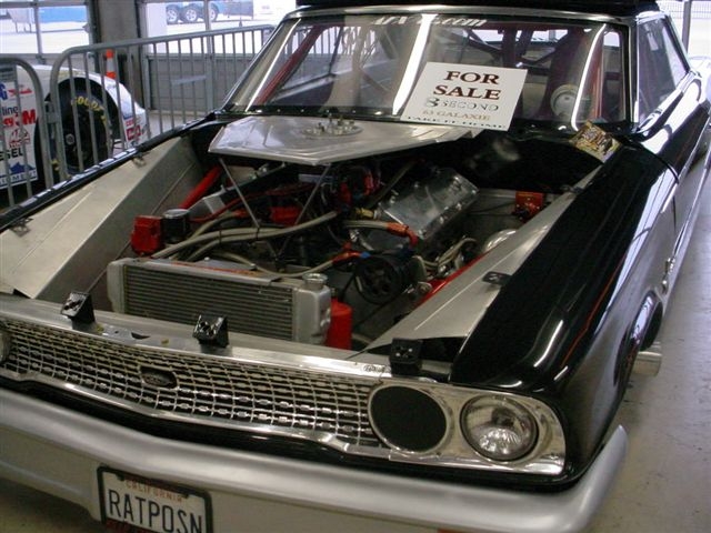 Front view of a black modified race car with engine exposed. License plate reads RATPOSN. Sign in window says 'FOR SALE'. Another race car visible in background