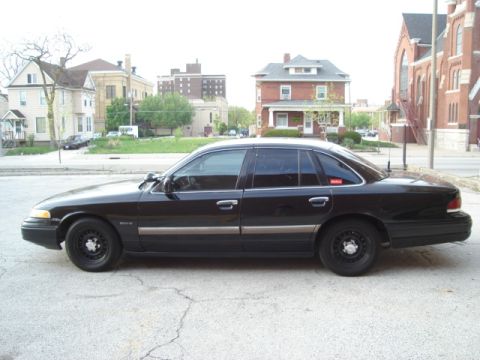 1992 Ford Crown Victoria - Side profile of a black 1992 Ford Crown Victoria sedan parked on a street with buildings in the background.