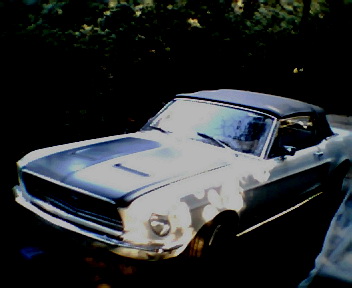 1968 Ford Mustang - A white 1968 Ford Mustang convertible with racing stripes on the hood is parked outside.