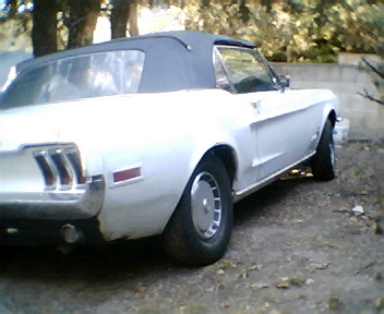1968 Ford Mustang - A white 1968 Ford Mustang convertible is viewed from the rear quarter, with a blue soft top and chrome accents visible.