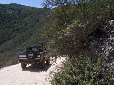 1991 Ford Bronco - A 1991 Ford Bronco navigates a dusty, off-road trail surrounded by arid hills and brush.