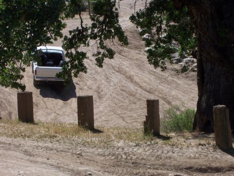1991 Ford Bronco - A white pickup truck navigates a dusty, off-road incline under the shade of trees.