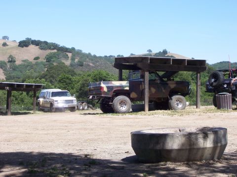 1991 Ford Bronco - Several trucks and a jeep are parked outdoors under a shelter on a sunny day.