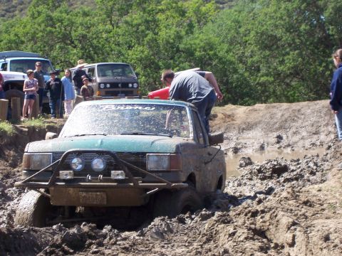 1991 Ford Bronco - A green Ford Bronco is stuck in a mud pit while other vehicles and people watch.