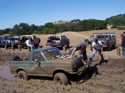 1991 Ford Bronco - Several vehicles are gathered around a muddy Bronco, with people attempting to free it from the mire.