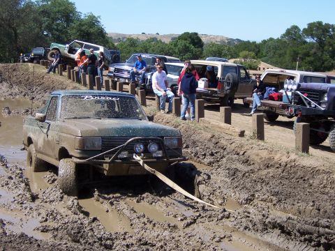1991 Ford Bronco - Several off-road vehicles navigate a muddy course with spectators watching.