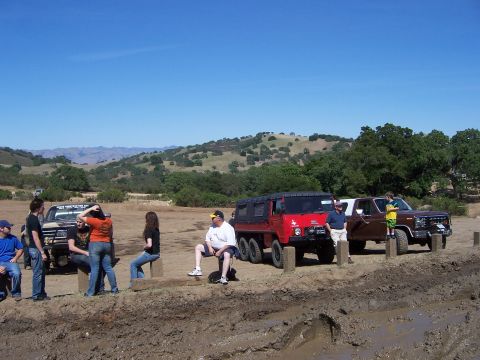 1991 Ford Bronco - Several vehicles and people gather in a muddy, rural landscape under a clear blue sky.