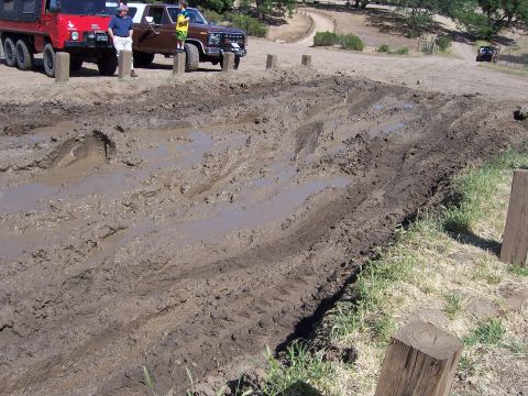1991 Ford Bronco - Two trucks are parked near a challenging muddy track during an off-road event.