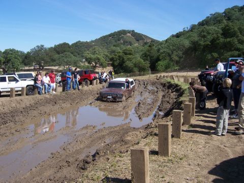 1991 Ford Bronco - Off-road enthusiasts watch as a vintage Ford Bronco navigates a challenging mud obstacle.