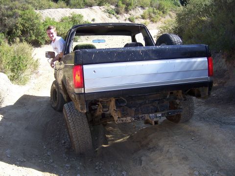 1991 Ford Bronco - A man smiles from the driver's seat of a black 1991 Ford Bronco as it navigates an off-road trail.
