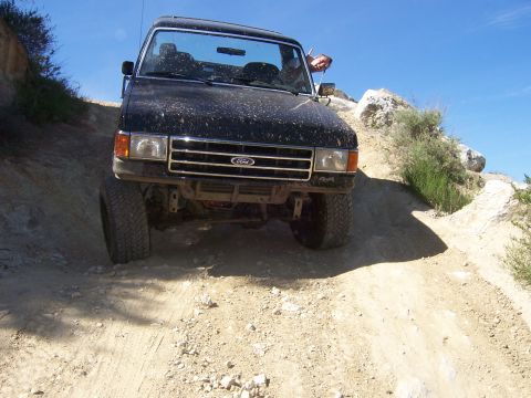 1991 Ford Bronco - A black 1991 Ford Bronco tackles a challenging off-road path under a clear blue sky.
