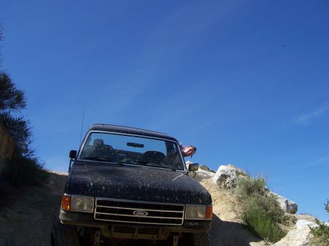 1991 Ford Bronco - This black Ford Bronco is navigating a rocky, off-road trail under a bright blue sky.