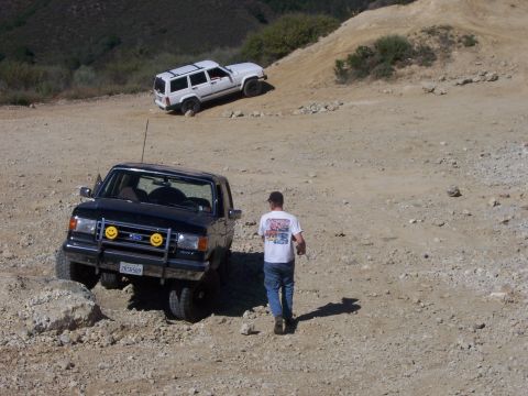 1991 Ford Bronco - A black 1991 Ford Bronco, equipped with distinctive smiley face headlights, tackles a challenging off-road course alongside another SUV.