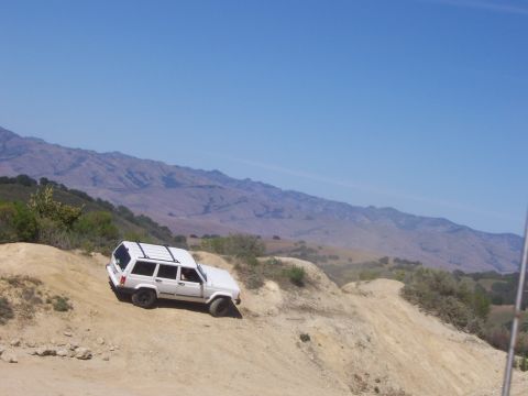 1991 Ford Bronco - A white Jeep Cherokee XJ navigates a steep dirt trail under a clear blue sky.
