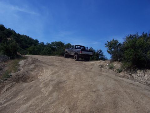 1991 Ford Bronco - A lifted Ford Bronco navigates a dusty trail under a clear blue sky.