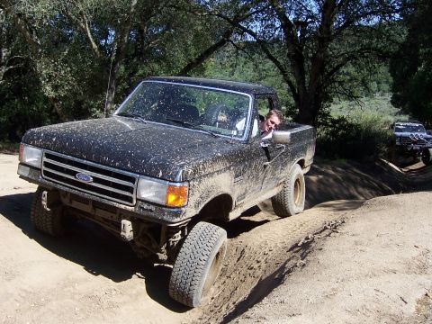 1991 Ford Bronco - A black Ford pickup truck navigates a muddy trail during an off-road event, with another vehicle visible in the background.
