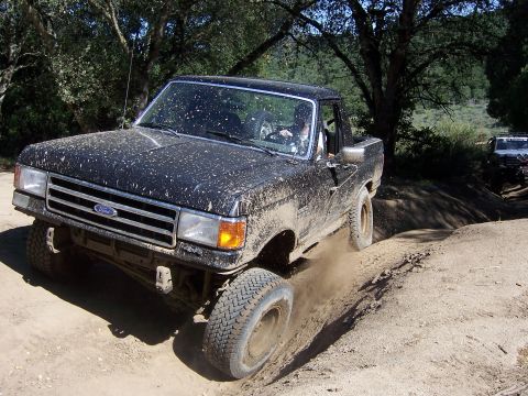 1991 Ford Bronco - Muddy 1991 Ford Bronco navigating an off-road trail with another vehicle visible in the background.