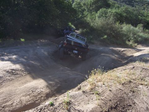 1991 Ford Bronco - A camouflaged pickup truck tackles a challenging off-road course, with another vehicle visible in the background.