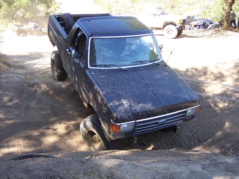 1991 Ford Bronco - A black pickup truck navigates a dirt track with another white truck in the background.