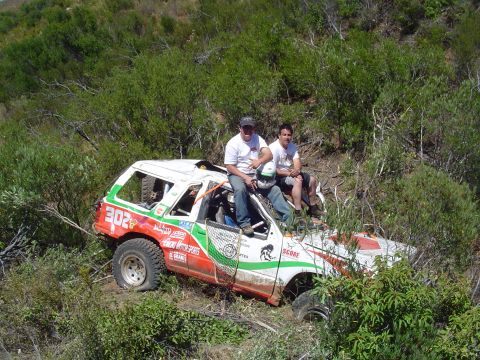 1992 Ford Explorer - Two men sit atop a damaged off-road vehicle in a wooded area, its tires deflated and bodywork compromised.