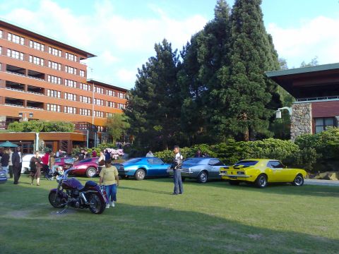 1991 Ford Crown Victoria - A collection of vintage cars and a motorcycle are displayed on a grassy area outside a large building.