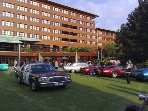 1991 Ford Crown Victoria - A 1991 Ford Crown Victoria police car is parked on a lawn with other vehicles and a large building in the background.