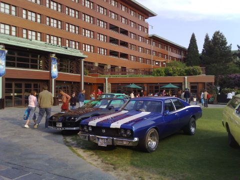 1991 Ford Crown Victoria - A blue 1973 Dodge Charger SE sedan is parked on the grass in front of a large wooden building.