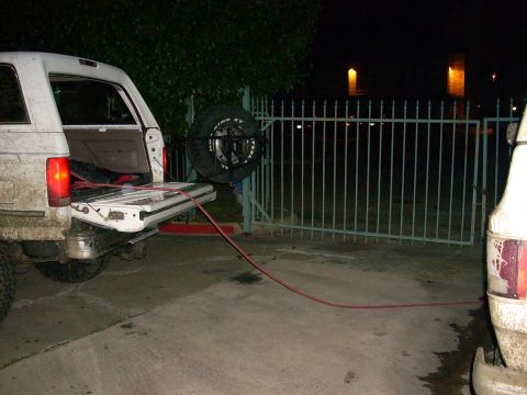 1992 Ford Bronco - A white SUV with its tailgate open and a spare tire mounted externally is parked near a metal fence at night.