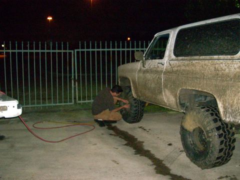 1992 Ford Bronco - Person works on a muddy SUV with large tires next to another vehicle.
