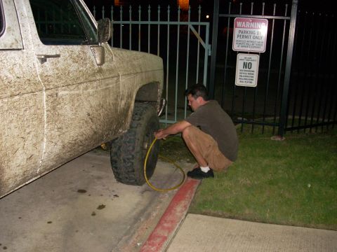 1992 Ford Bronco - A man is airing up the tire of a very muddy truck next to a fence with warning signs.