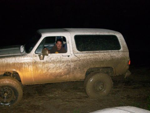 1992 Ford Bronco - A white SUV is heavily covered in mud, with the driver visible behind the wheel.