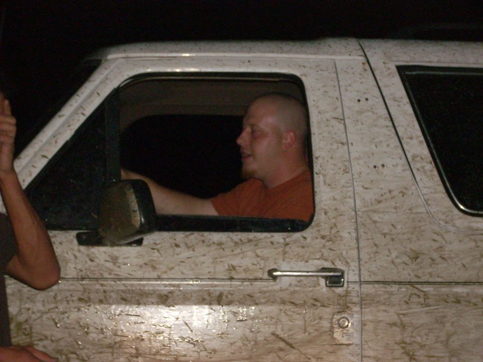 Guy driving a white SUV covered in mud. Another person's arm is visible on the left