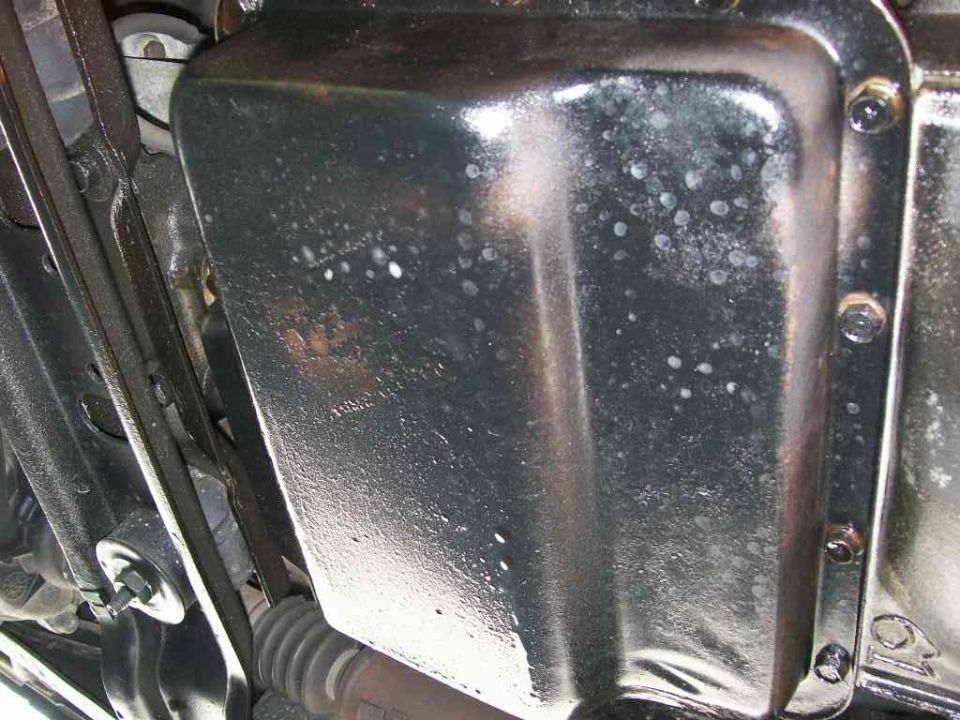 Black steel oil pan underside with flange bolts, rust patch and white spatter