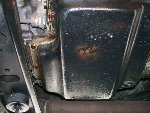 1984 Ford Bronco - Underside view of a vehicle's oil pan and transmission linkage, showing some rust and oil residue.